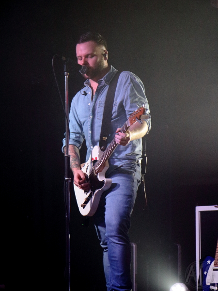 A solitary guitarist on stage singing into a microphone.