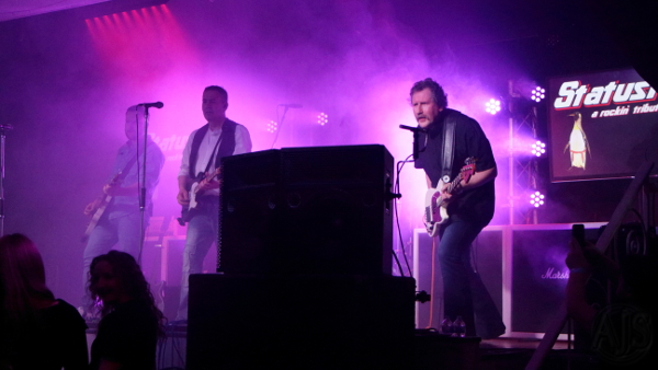 Purple lit dry ice filled stage with the three Status Faux guitarists looking out into the audience.