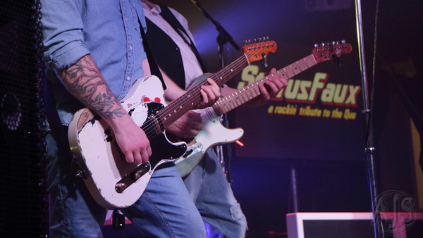Close up of the two Status Faux front men in a row playing guitar with backdrop visible.