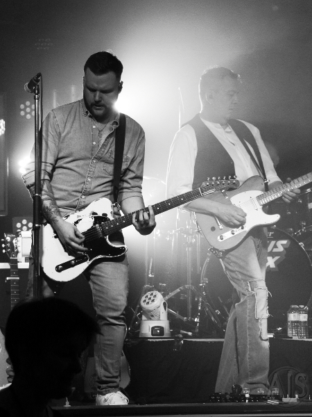 Two Status Faux guitarists on a dry ice filled stage lit from behind.