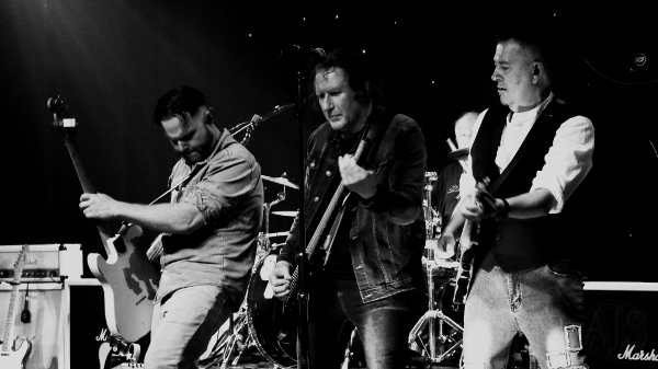 Three guitarists in a row performing together on stage.